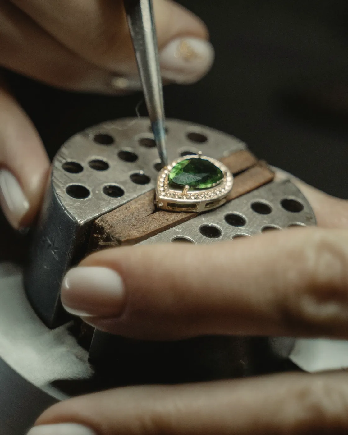 A jeweler’s hands setting a stone into a ring on a bench clamp