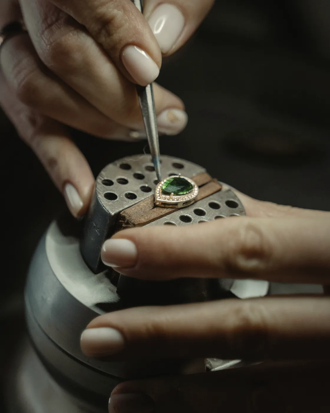 A jeweler’s hands setting a stone into a ring held in a bench clamp
