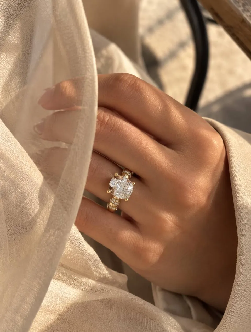 The finished Station Halo on a hand: 18K yellow gold, cushion center, pavé stations, in daylight against cream fabric